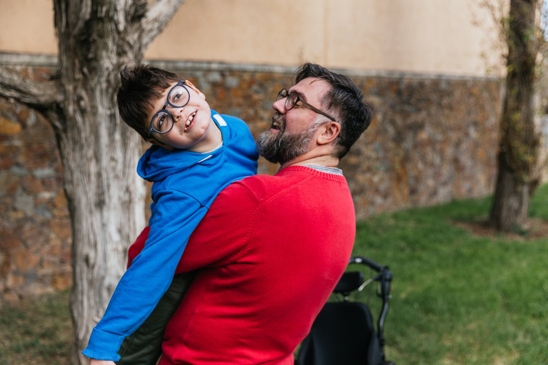 Man Holding and Playing with His Son with Disability While Enjoying Good Time Together Outdoors.